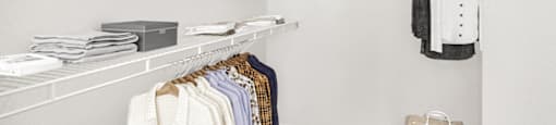 A vacant walk-in closet with carpet throughout, white walls, and white wired shelving installed on either side of the closet.