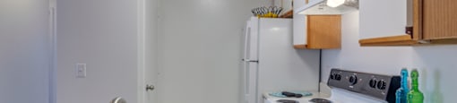 The three bedroom kitchen has white cabinets with tan trim, white appliances, formica countertops, and a double basin sink with gooseneck faucet.