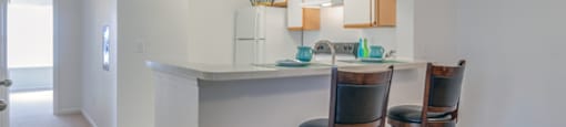 The three bedroom kitchen features a breakfast bar, white cabinets with tan trim, and white appliances. This mini model has two barstools at the breakfast bar.