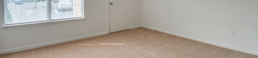 The vacant bedroom has wall to wall carpet, a large picture window and a door leading to a closet.