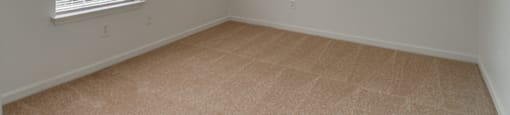 The vacant bedroom has wall to wall carpet, white walls and a standard window on one of the walls.