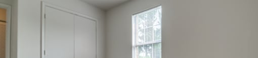 The vacant bedroom has wall to wall carpet, white walls, one standard window, and double doors opening to the closet.
