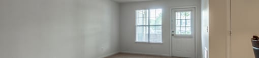 The vacant apartment living room has wall to wall carpet white walls, large picture window and a door leading out to the patio.