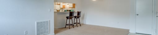 The living and dining room has carpet with linoleum flooring in the entry. There is breakfast bar that opens to the kitchen. This mini model is furnished with two barstools positioned at the breakfast bar.