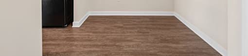 A black refrigerator sits in a room with wooden floors and white walls.