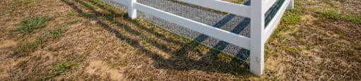 A white fence in a field with buildings in the background.