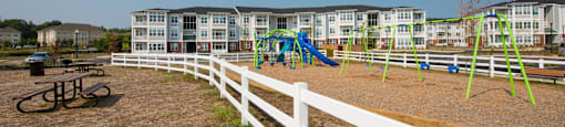 A playground with a white fence and a green slide.