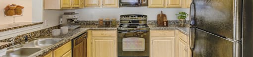 a kitchen with wood cabinets and black appliances at Stone Gate Apartments, Spring Lake, NC