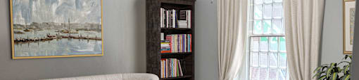 a living room with a couch coffee table, bookshelf, and a window
