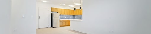 A large empty room with a kitchenette in the background.