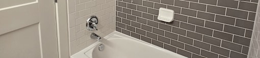 A white bathtub in a bathroom with grey tiles.