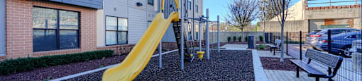A playground with a yellow slide in front of a building.