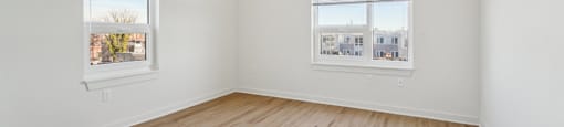 A room with wooden flooring and two windows.