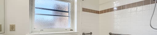 A white sink is on the left side of a bathroom with a window and a bathtub.