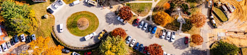 An aerial view of a campus with a large building in the center and a parking lot with cars.