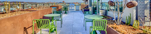 A patio with green chairs and a table is surrounded by a wall and a building.