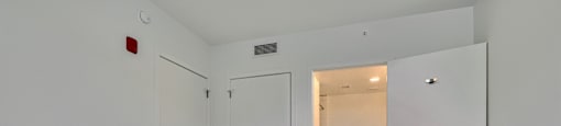 A room with white walls and a wood floor with a door on the left and one open to a hallway.