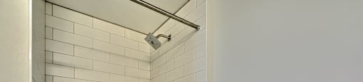 A white tiled shower area with a shower head and hand held shower.