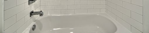 A white tiled bathroom with a white bathtub and a shower head.