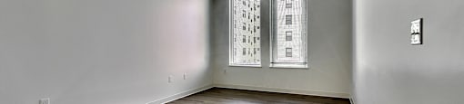 A room with wooden flooring and two windows.