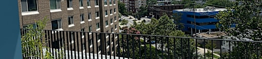 A balcony with a black railing and potted plants overlooks a cityscape.