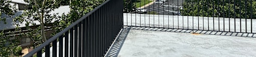A balcony with a black railing overlooks a street with cars and houses.