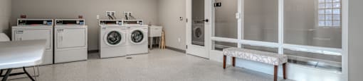 a laundry room with washes and dryers and a table with a bench