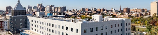 A large white building with a blue stripe on the side is in the foreground of a cityscape.
