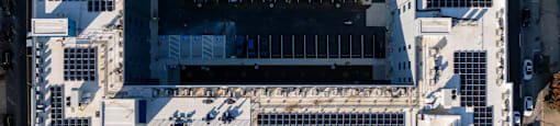 An aerial view of a large white building with a lot of windows and a parking lot in front.