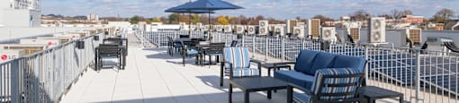 A rooftop patio with a white tile floor and black chairs and tables.