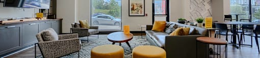 A living room with a grey couch, a yellow ottoman, and a television.