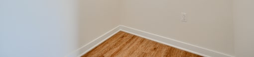Empty room with a white wall and a wooden floor.