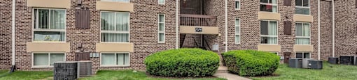 a brick apartment building with green grass and a sidewalk