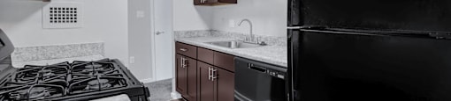 a kitchen with black appliances and marble counter tops and dark wood cabinets