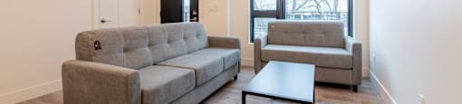 A grey couch and a grey chair are in a room with a window.