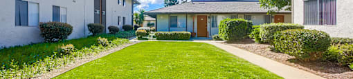 a pathway between two houses with a green lawn and a sidewalk