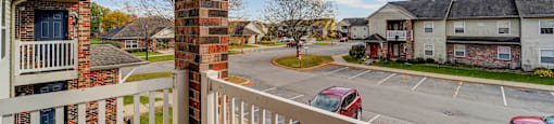 A view from a balcony overlooking a parking lot and other buildings.