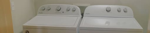 Two white front loading washing machines in a small laundry room.