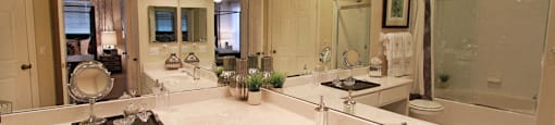 Luxury apartments with white cabinets, linen closet, extra cabinet space, cultured marble vanity, built-in vanity, roman tub with glass door and shower, and porcelain tiled floor at The Biltmore Apartments in Omaha, Nebraska
