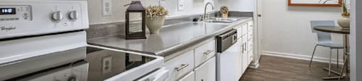 Bright white kitchen with wood plank floors, extra cabinet space and counter space at Woodlake on the Bayou Apartments
