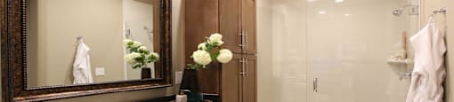 Spacious bathroom with built-in shelves, frameless glass walk-in shower, and granite slab vanity top Tuscany Walk Apartments in Houston.