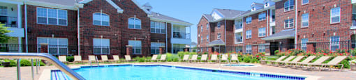 Luxury apartments with red brick exteriors, swimming pool, pool-side lounge chairs, beautiful landscaping, and scenic views at Rockledge Oaks Apartments in Lincoln, Nebraska