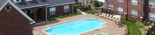 Luxury apartments with red brick exteriors, swimming pool, pool-side lounge chairs, beautiful landscaping, and scenic views at Rockledge Oaks Apartments in Lincoln, Nebraska