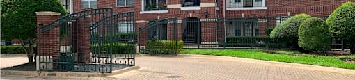 Gated community luxury apartments with brick exteriors, private outside storage, French doors, and lush landscaping including beautiful chaste trees at Tuscany Apartments in Houston.