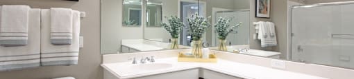 Luxury bathroom with tiled floors, glass shower, oval soaking tub, cultured marble vanity, and white cabinets in at Rockledge Oaks Apartments in Lincoln, Nebraska