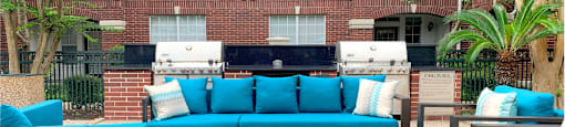 Luxury apartments with brick exteriors, pool-side lounge seating, and grilling area at Tuscany Apartments in Houston.