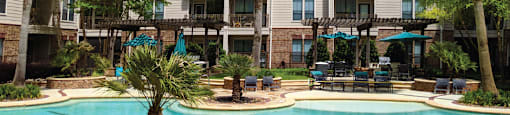 Luxury swimming pool with cabanas, poolside lounges, grilling stations, palm trees and beautiful landscaping at The Voss Apartments in Houston.