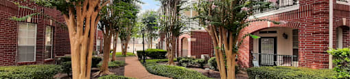Luxury apartments with brick exteriors and lush landscaping including beautiful chaste trees at Tuscany Apartments in Houston.