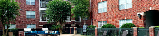 Luxury apartments with red brick exteriors, large swimming pool with spacious sundeck, grill, beautiful landscaping, lush landscaping, chaste trees, and pool-side lounge seating at Tuscany Apartments in Houston.