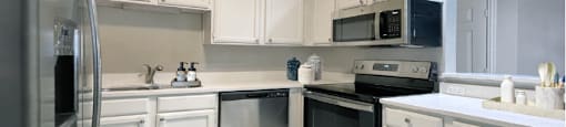 Spacious bright white kitchen with white cabinets, stainless steel appliances, side-by-side refrigerator, and tiled floor at Prestonbridge Apartments in North Dallas